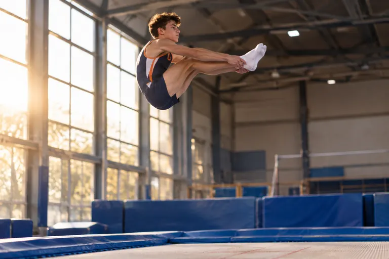 Un adolescent en plein saut carpé au-dessus d'un trampoline de compétition